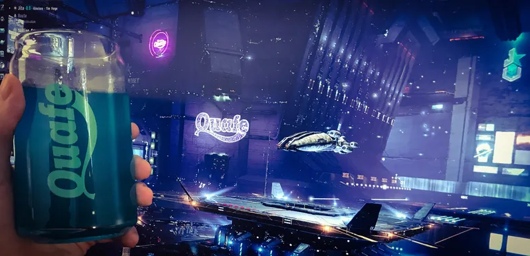 A capsuleer toasts with a real glass of green Quafe in front of EVE's Jita 4-4 station, the in-game Quafe billboard glowing behind.